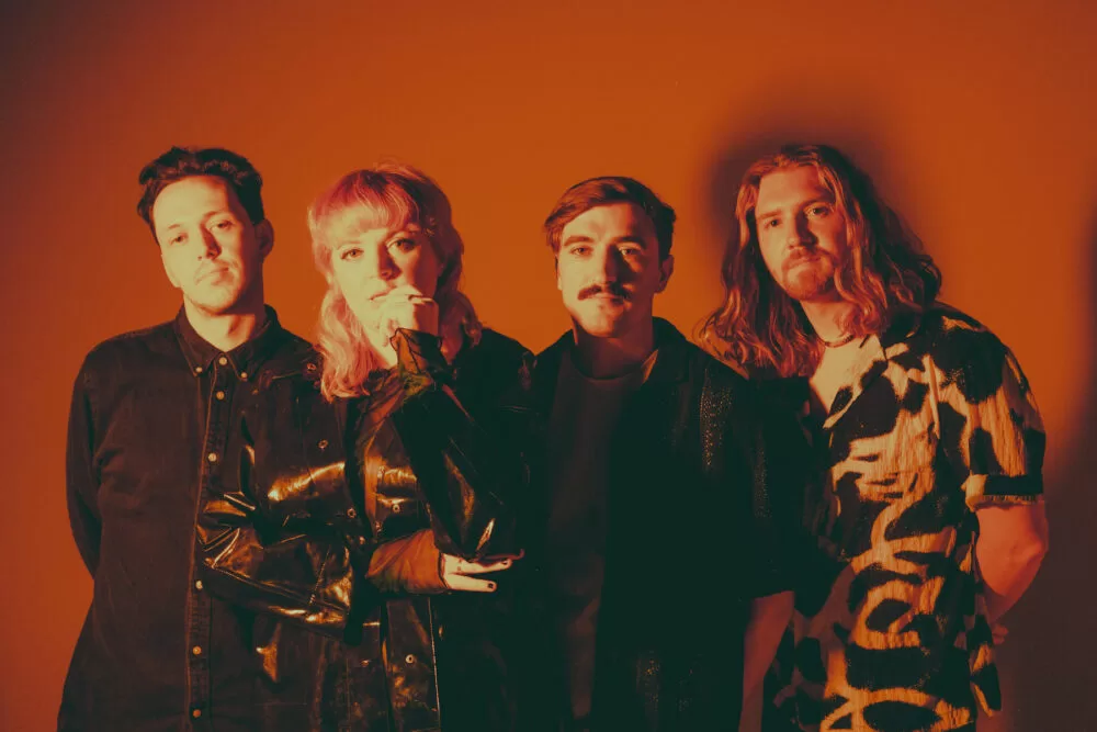 SPRINTS - "Letter to Self": A Defiant Declaration of Intent 2 The band Sprints posing in front of an orange background